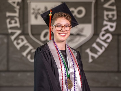 Grace Moon posing in front of CSU seal wearing valedictorian stole and commencement regalia. 