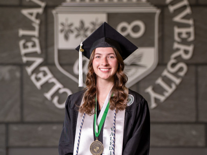 Sarah McCartney posing in front of CSU seal wearing valedictorian stole and commencement regalia. 