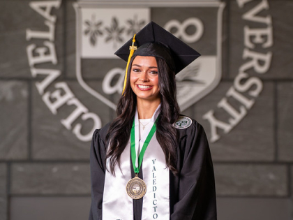 Sydney Wisnor posing in front of CSU seal wearing valedictorian stole and commencement regalia. 