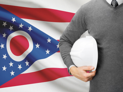 Ohio flag with a worker holding a hard hat standing next to it.